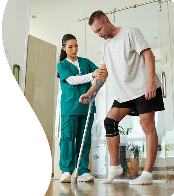 Physical therapist assisting a man with a knee brace during rehabilitation exercises in a clinic.
